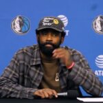 Kyrie Irving watches Dallas Mavericks teammates test drive custom golf carts during a holiday team gift moment.