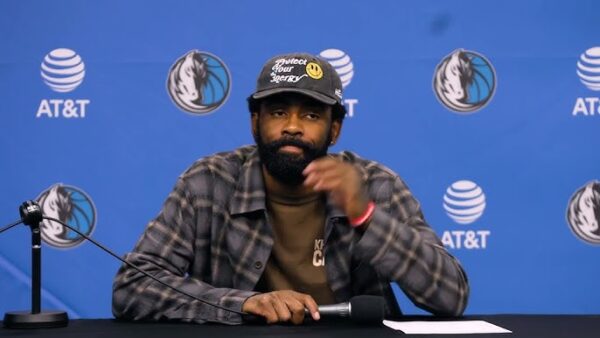 Kyrie Irving watches Dallas Mavericks teammates test drive custom golf carts during a holiday team gift moment.