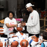 Bam Adebayo stands on the court at Kaseya Center surrounded by children and tables filled with holiday toys during a large community giveaway.