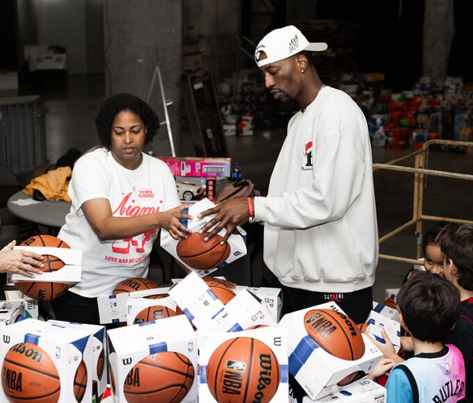Bam Adebayo stands on the court at Kaseya Center surrounded by children and tables filled with holiday toys during a large community giveaway.